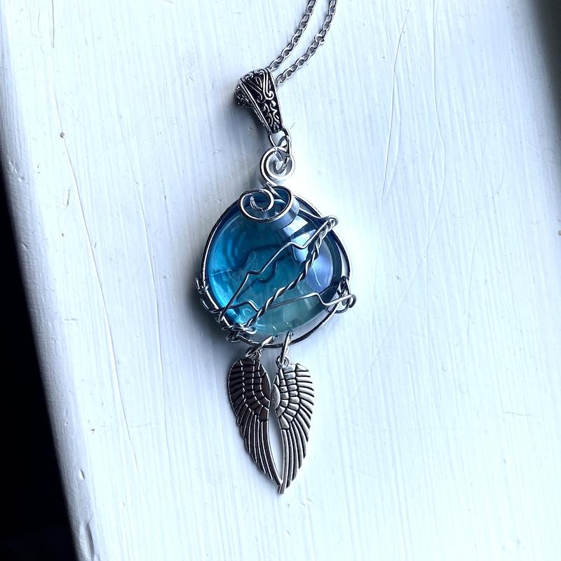 A necklace with a blue glass circle wire wrapped with angel wings beneath it.