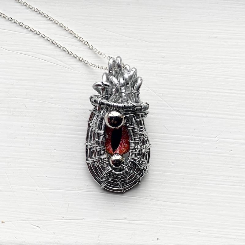 A necklace consisting of an orange red cat's eye, surrounded in an intricately woven framework