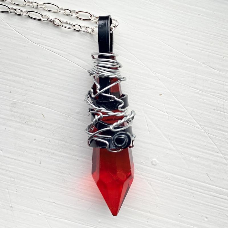 A necklace consisting of a red crystal point wire wrapped in black and silver wire