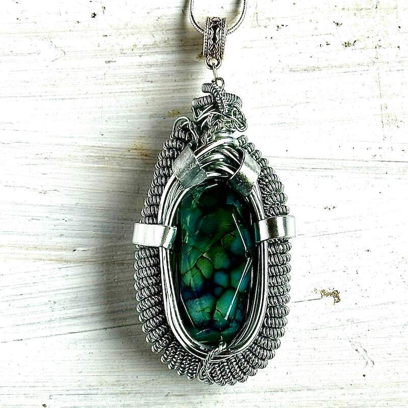An oval shaped necklace with a green speckled agate that has been intricately wire wrapped in silvver wire