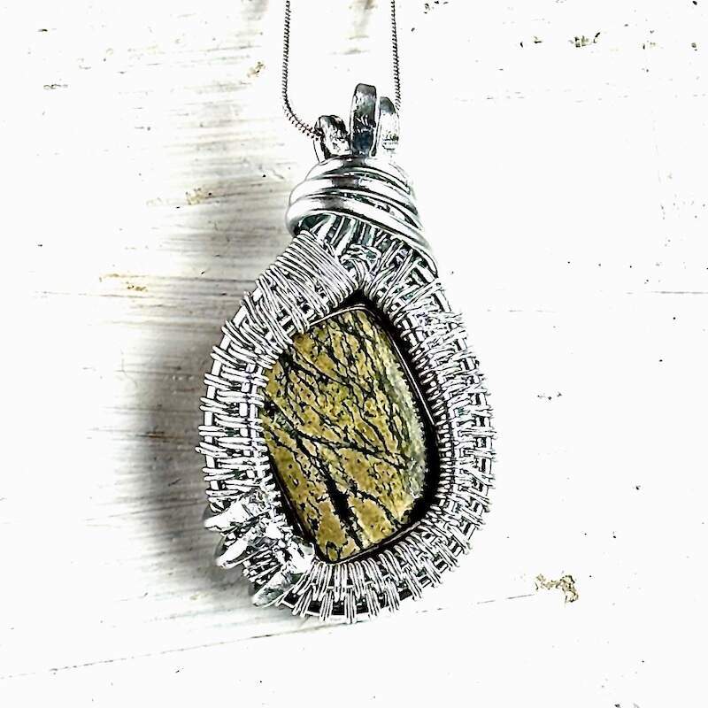A teardrop shaped necklace with an intricate wire weaving style and a rainforest jasper focal