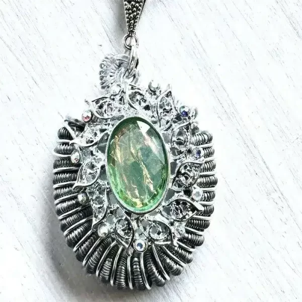 A necklace made of a silver focal with greens and golds over a wire wrapped coil element