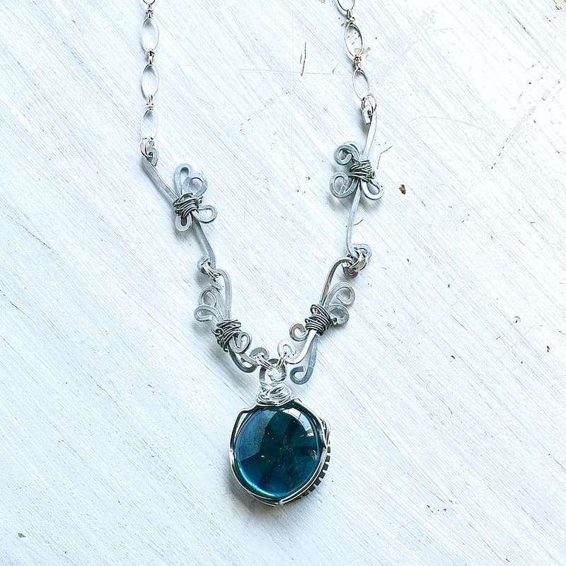 A necklace with a round blue glass focal and coiled wirework forming the chain