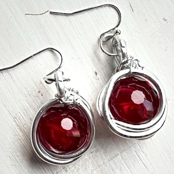 Red faceted glass earrings that are round and wrapped in silver wire