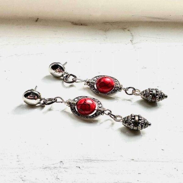 Silver and red earrings. The earrings are stud earrings. They are long with red and black beads which are inside pewter bead cages. Underneath that hang sterling silver medieval inspired beads.